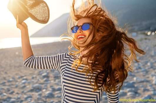 Frau am Strand mit wehenden Haaren und Sonnenhut